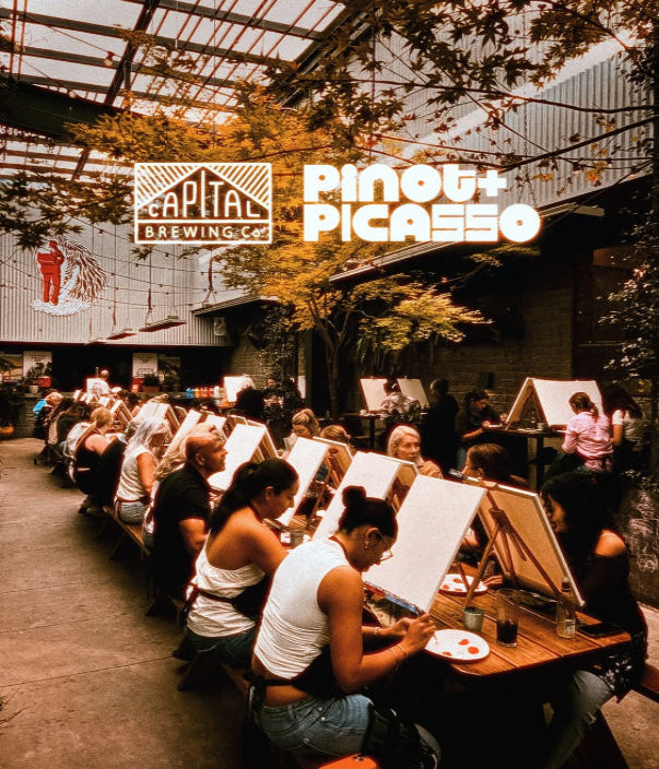 People sitting at tables with art supplies in an outdoor setting, featuring Capital Brewing Co. and Pinot + Picasso logos.